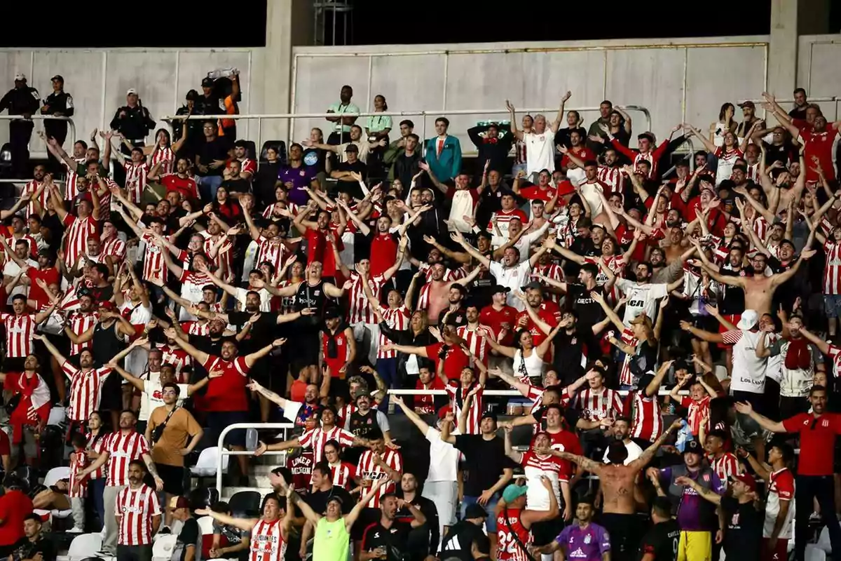 Aficionados de fútbol con camisetas rojas y blancas celebran y animan en las gradas de un estadio Aficionados de fútbol con camisetas rojas y blancas celebran y animan en las gradas de un estadio