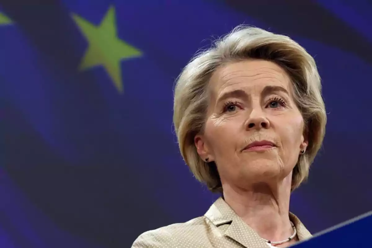 Short-haired blonde woman with a serious expression in front of a blue flag with yellow stars Short-haired blonde woman with a serious expression in front of a blue flag with yellow stars