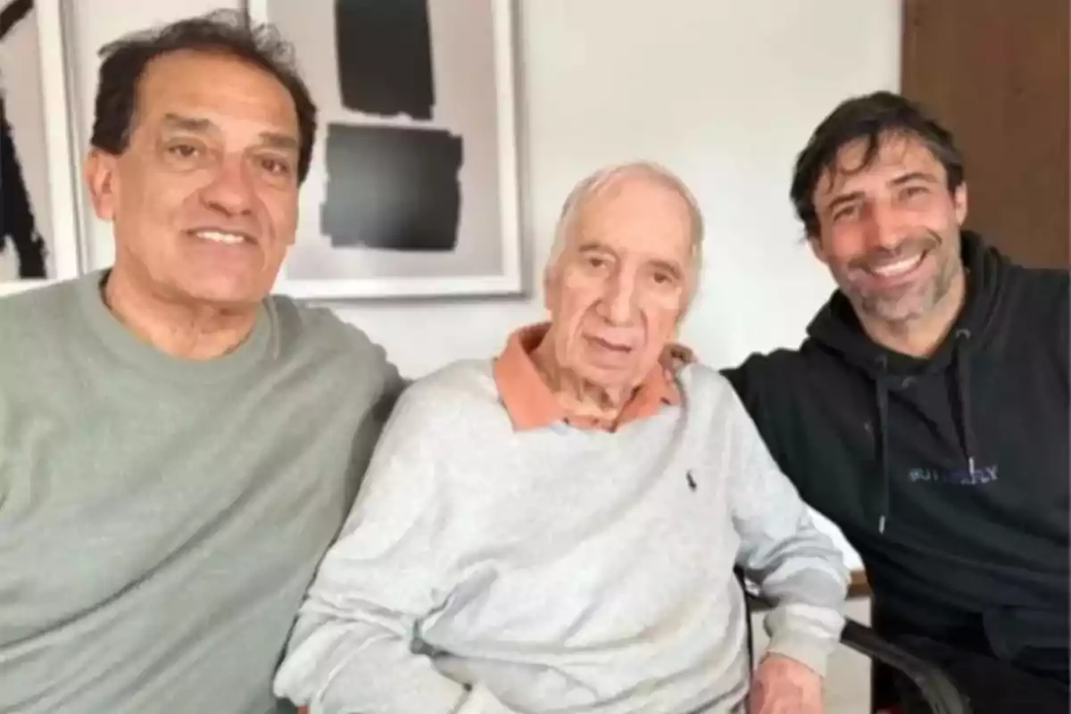 Tres hombres de diferentes edades posan juntos y sonríen en una habitación iluminada Tres hombres de diferentes edades posan juntos y sonríen en una habitación iluminada