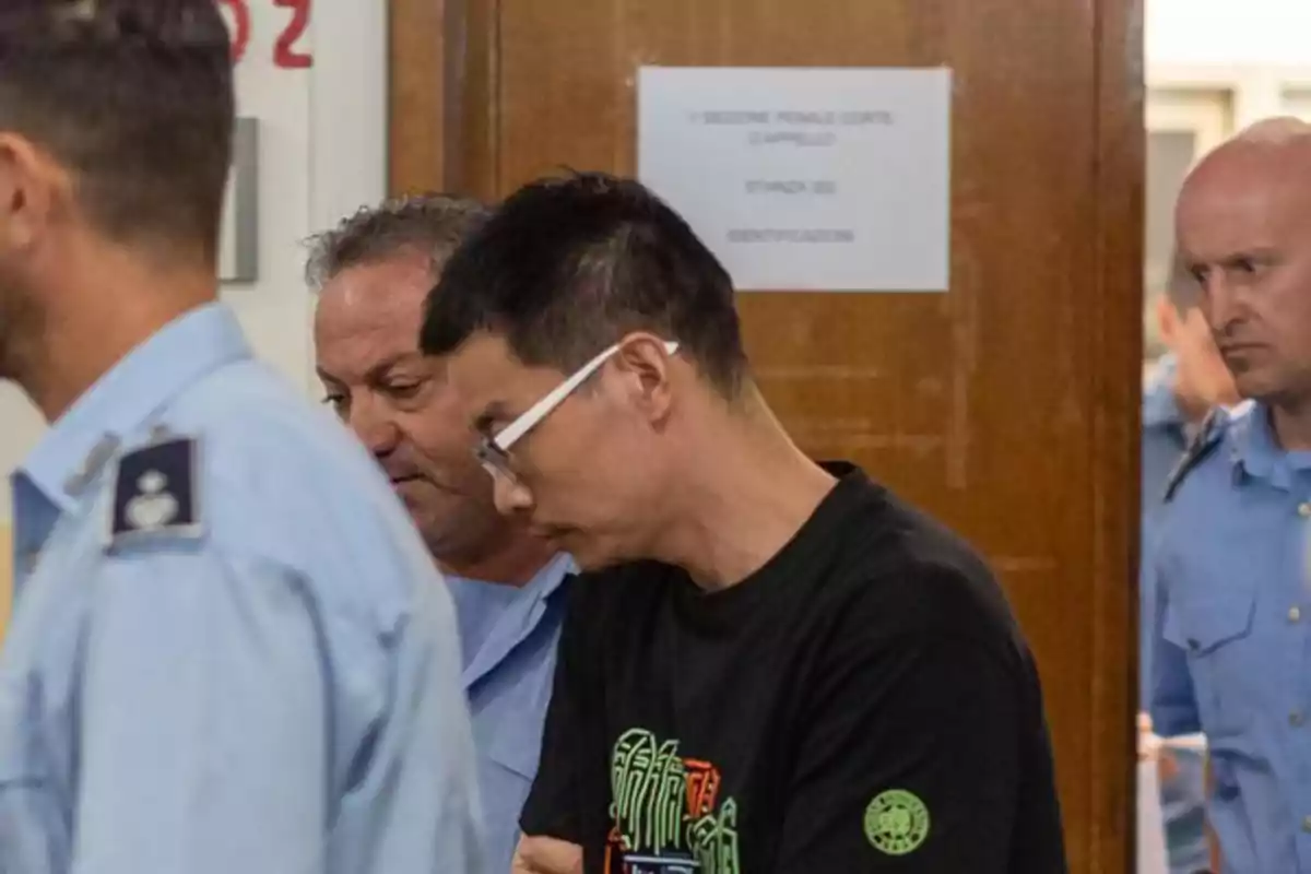 A man escorted by police officers inside a building with wooden doors and a sign on the wall in the background A man escorted by police officers inside a building with wooden doors and a sign on the wall in the background
