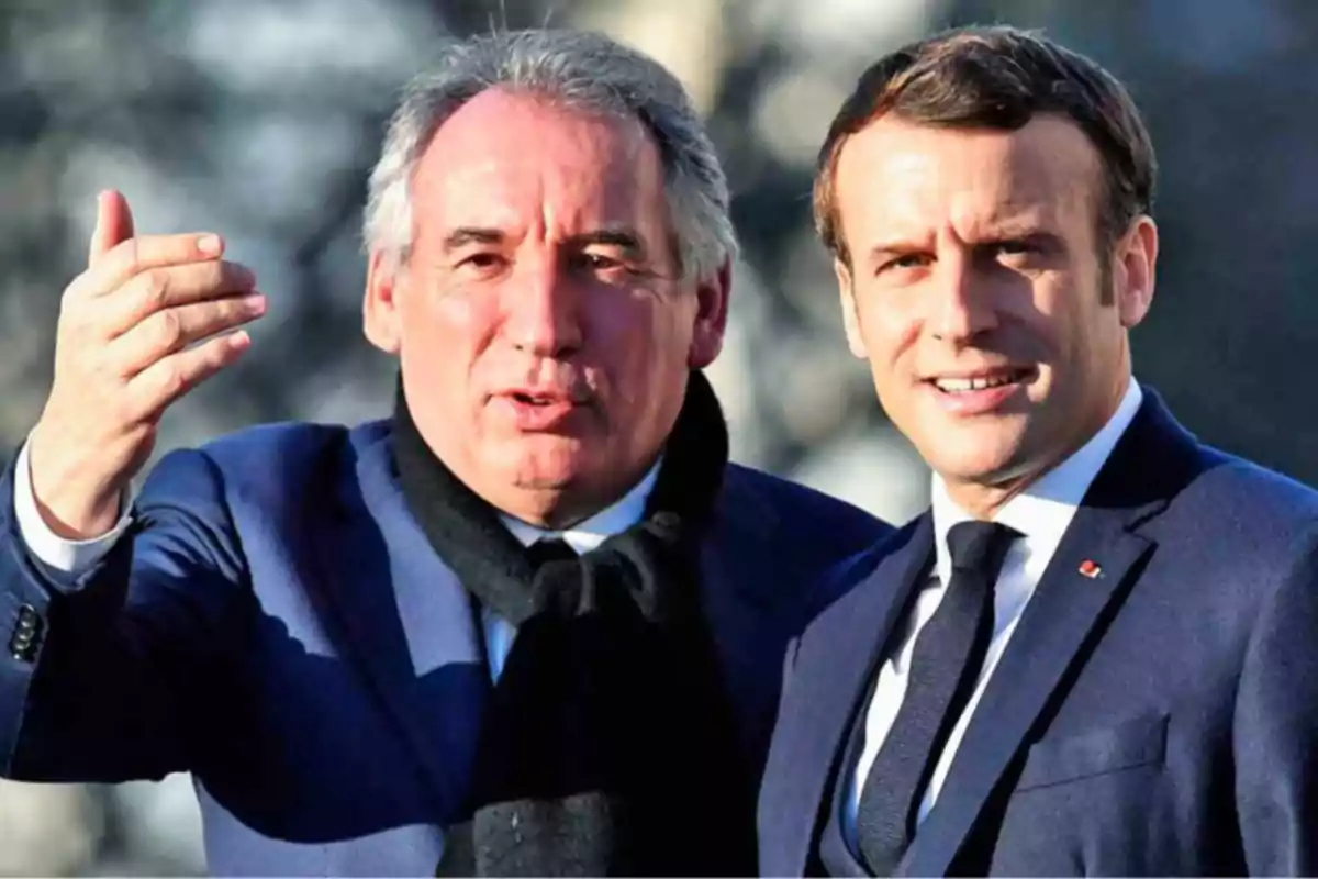Dos hombres vestidos con traje oscuro posan juntos al aire libre, uno de ellos sonríe mientras el otro gesticula con la mano. Dos hombres vestidos con traje oscuro posan juntos al aire libre, uno de ellos sonríe mientras el otro gesticula con la mano.