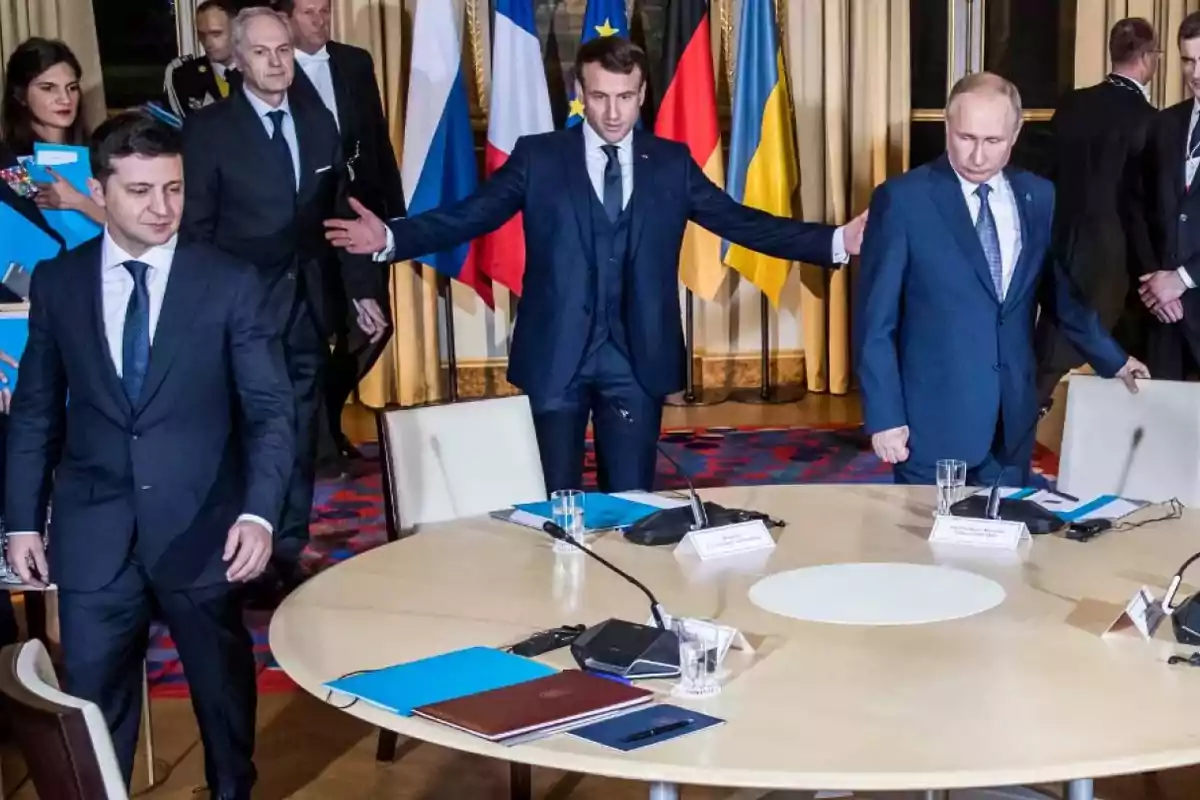 Three men in suits are getting ready to sit at a round conference table, with flags from several countries in the background. Three men in suits are getting ready to sit at a round conference table, with flags from several countries in the background.