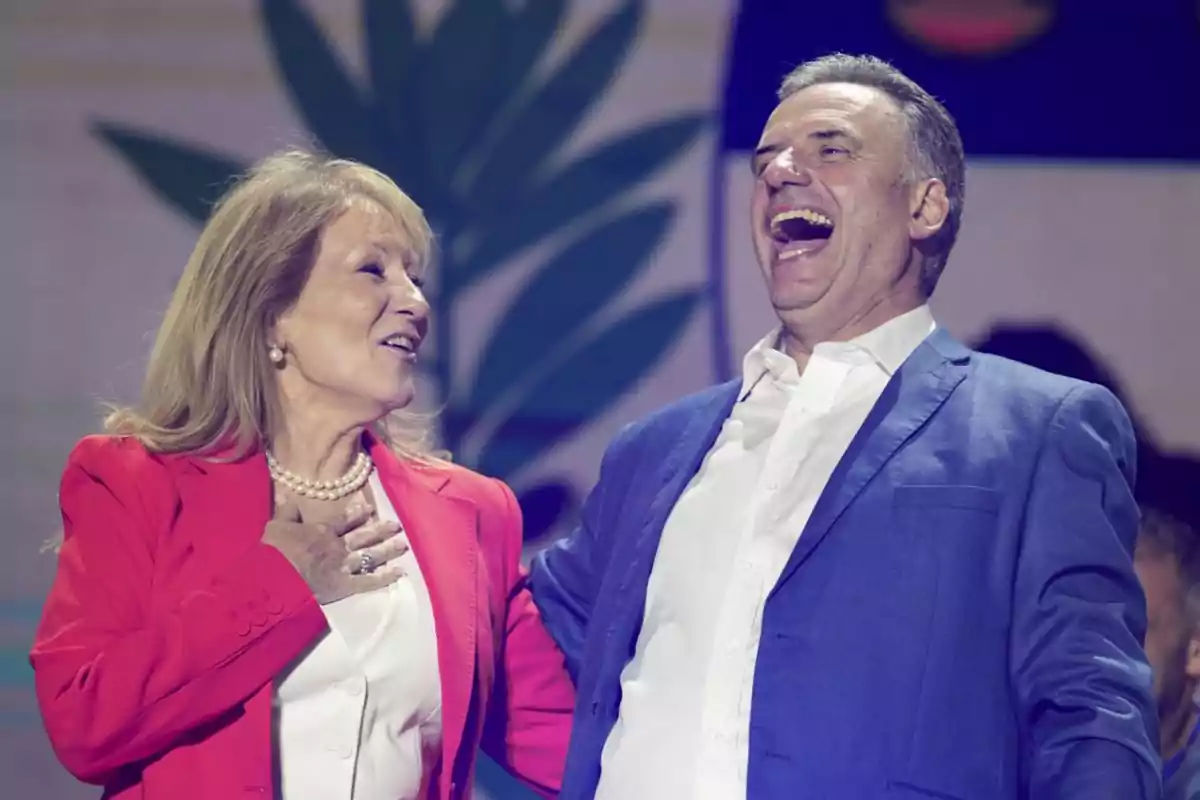 A woman and a man elegantly dressed smile and share a moment of joy on a brightly lit stage.
