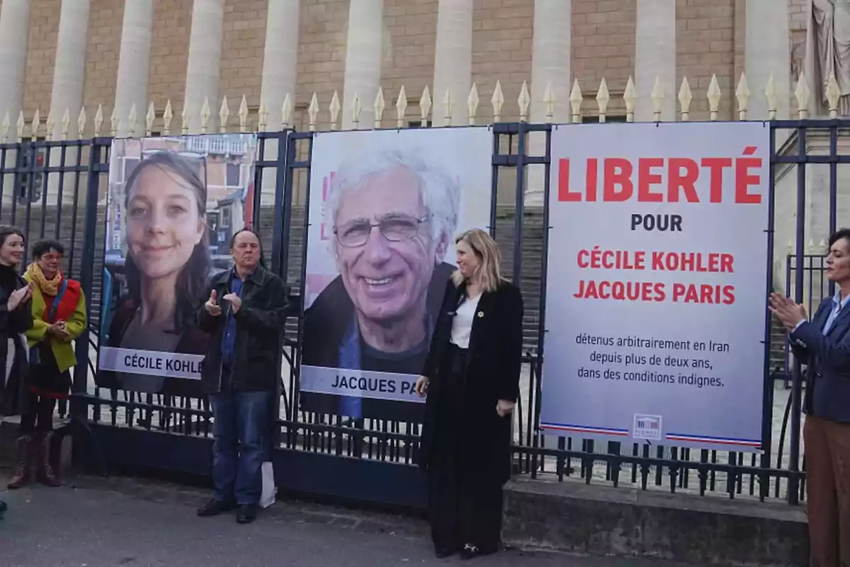 Varias personas están reunidas frente a una reja donde hay carteles grandes con las fotos de Cécile Kohler y Jacques Paris junto a un cartel que pide libertad para ellos y menciona que están detenidos en Irán Varias personas están reunidas frente a una reja donde hay carteles grandes con las fotos de Cécile Kohler y Jacques Paris junto a un cartel que pide libertad para ellos y menciona que están detenidos en Irán