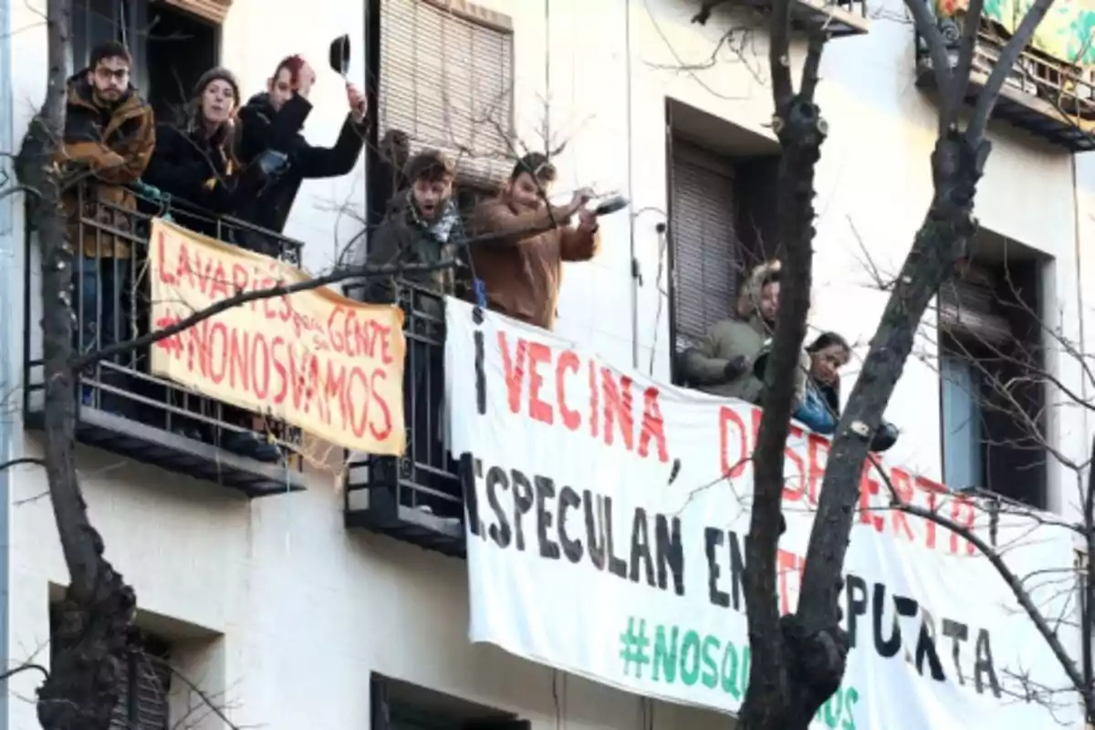 Personas en un balcón protestando con cacerolas y pancartas que dicen Lavapiés para su gente #nonosvamos y Vecina despierta especulan en tu puerta #nosquedamos