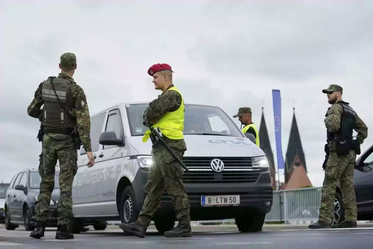 Cuatro soldados con uniforme de camuflaje y chalecos de seguridad revisan vehículos en un control fronterizo junto a una furgoneta blanca Volkswagen