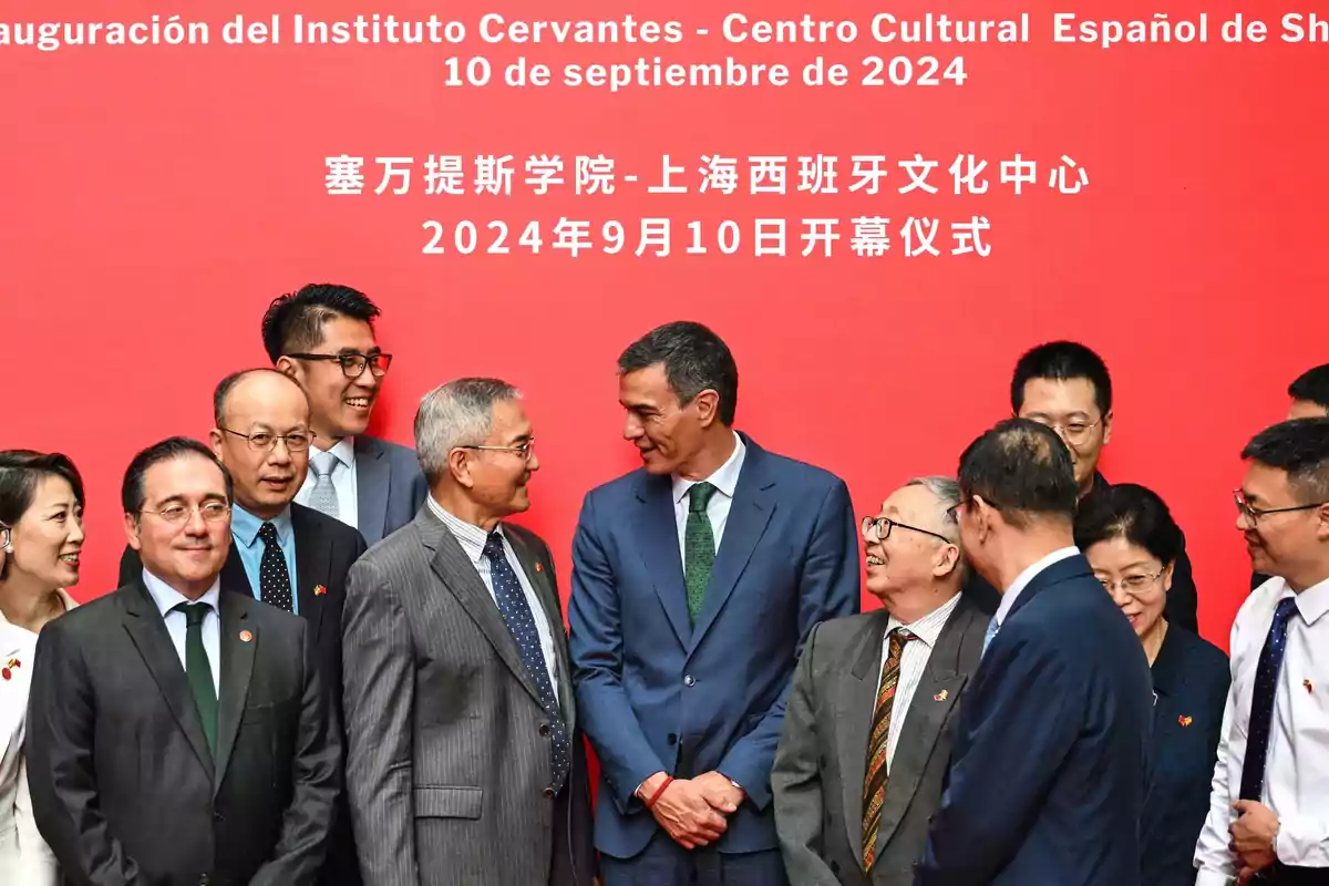 Grupo de personas sonríe y conversa frente a un fondo rojo con texto en español y chino durante un evento oficial Grupo de personas sonríe y conversa frente a un fondo rojo con texto en español y chino durante un evento oficial