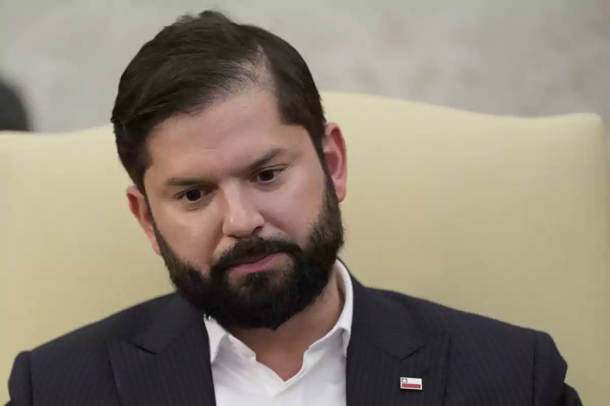 Hombre de barba y cabello oscuro con expresión seria sentado en una silla clara y usando un traje oscuro con camisa blanca Hombre de barba y cabello oscuro con expresión seria sentado en una silla clara y usando un traje oscuro con camisa blanca