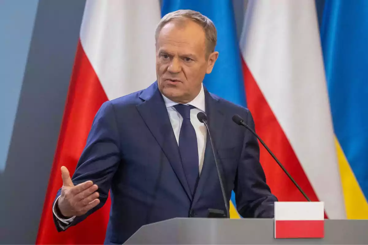 Man in a blue suit speaking at a podium with microphones and the flags of Poland and Ukraine in the background Man in a blue suit speaking at a podium with microphones and the flags of Poland and Ukraine in the background