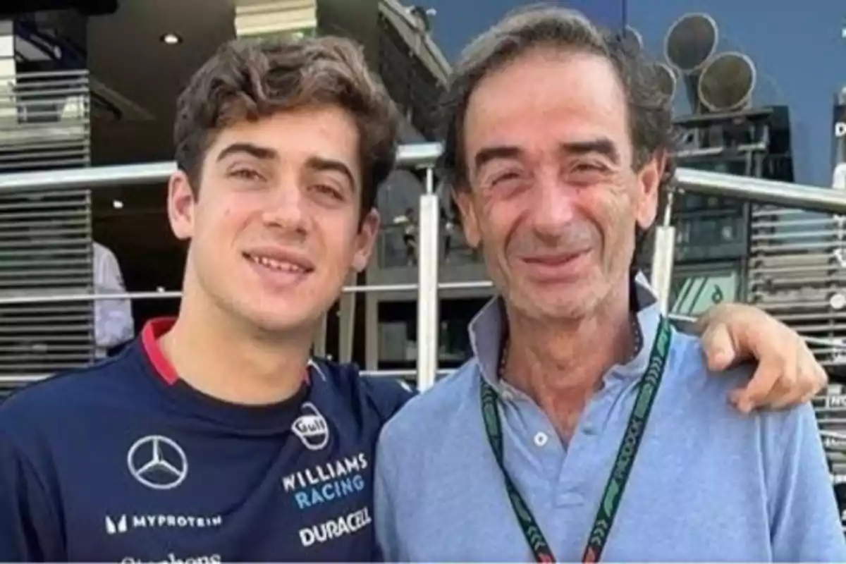 Dos personas sonríen y posan juntas al aire libre, una de ellas lleva una camiseta de Williams Racing y la otra una camisa azul claro.