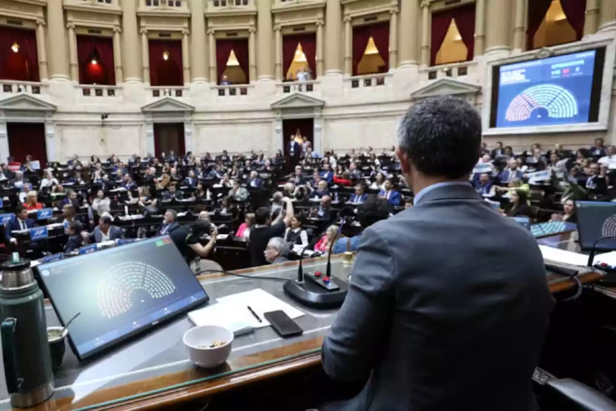 View from the podium of a parliamentary chamber with many people seated at their desks and screens displaying voting results View from the podium of a parliamentary chamber with many people seated at their desks and screens displaying voting results