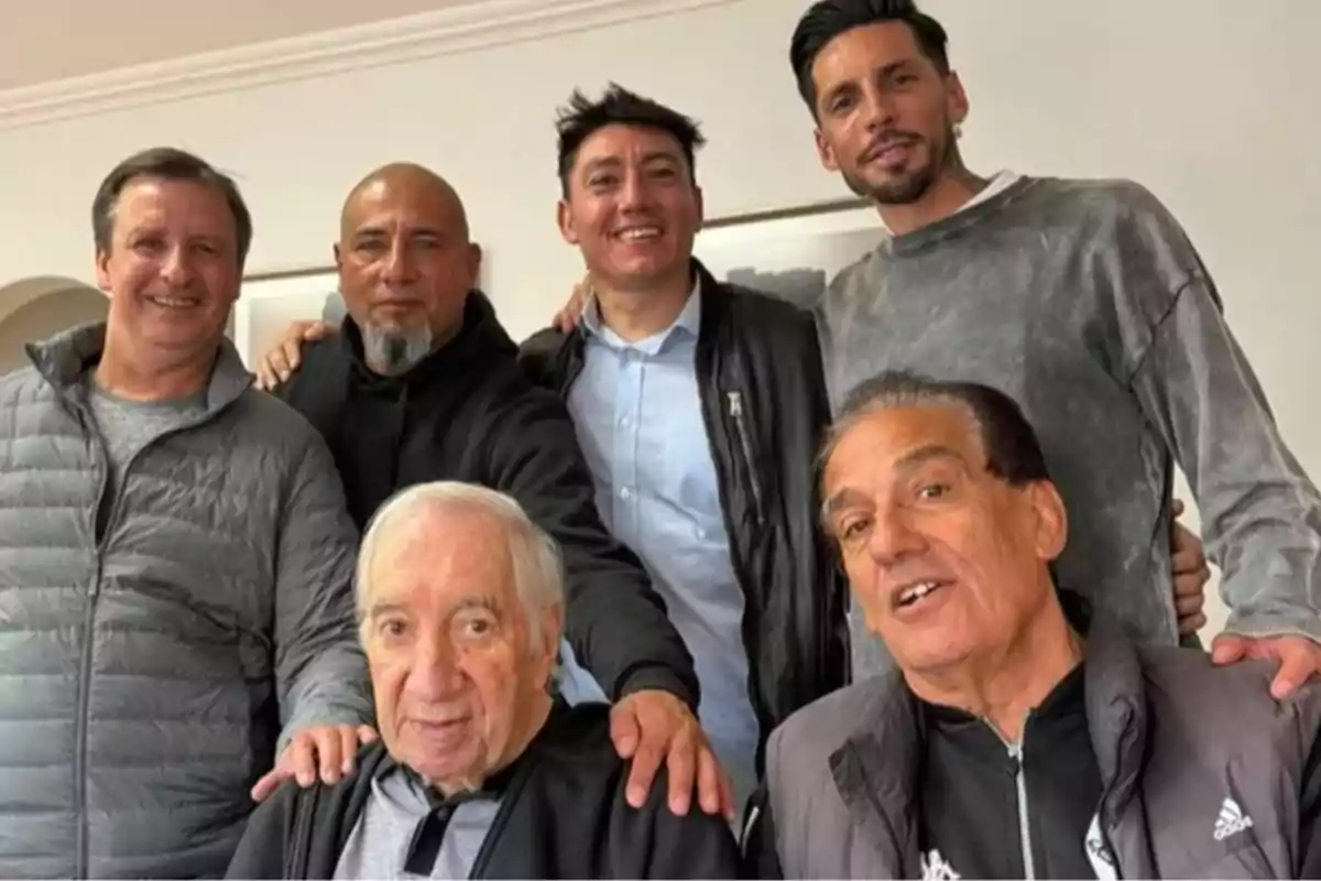 Seis hombres posan juntos y sonríen en una habitación iluminada Seis hombres posan juntos y sonríen en una habitación iluminada