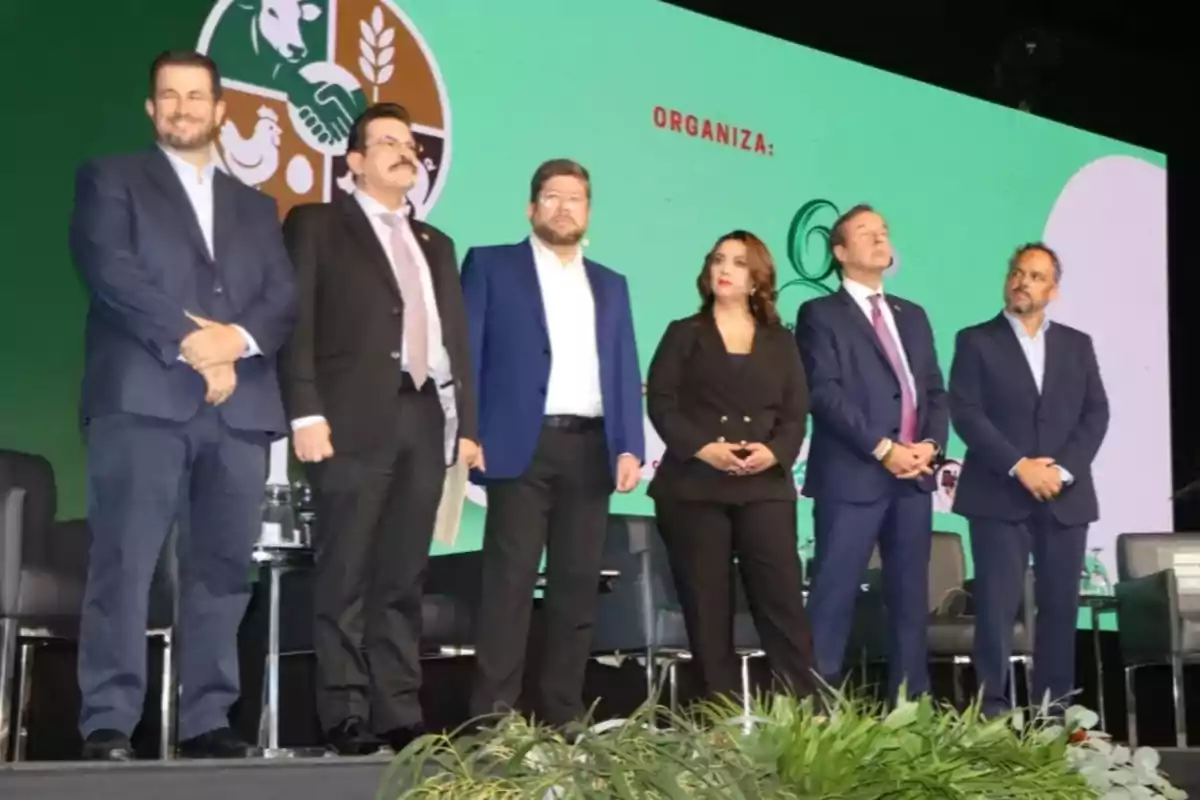 Six people standing on a stage during a formal event with a green background and a logo related to agriculture and livestock. Six people standing on a stage during a formal event with a green background and a logo related to agriculture and livestock.