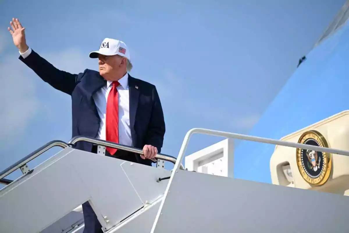Hombre con traje y gorra blanca saludando mientras sube las escaleras de un avión presidencial Hombre con traje y gorra blanca saludando mientras sube las escaleras de un avión presidencial