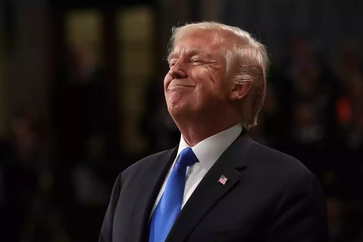 Blond-haired man in a dark suit and blue tie smiling with a satisfied expression in a formal setting Blond-haired man in a dark suit and blue tie smiling with a satisfied expression in a formal setting