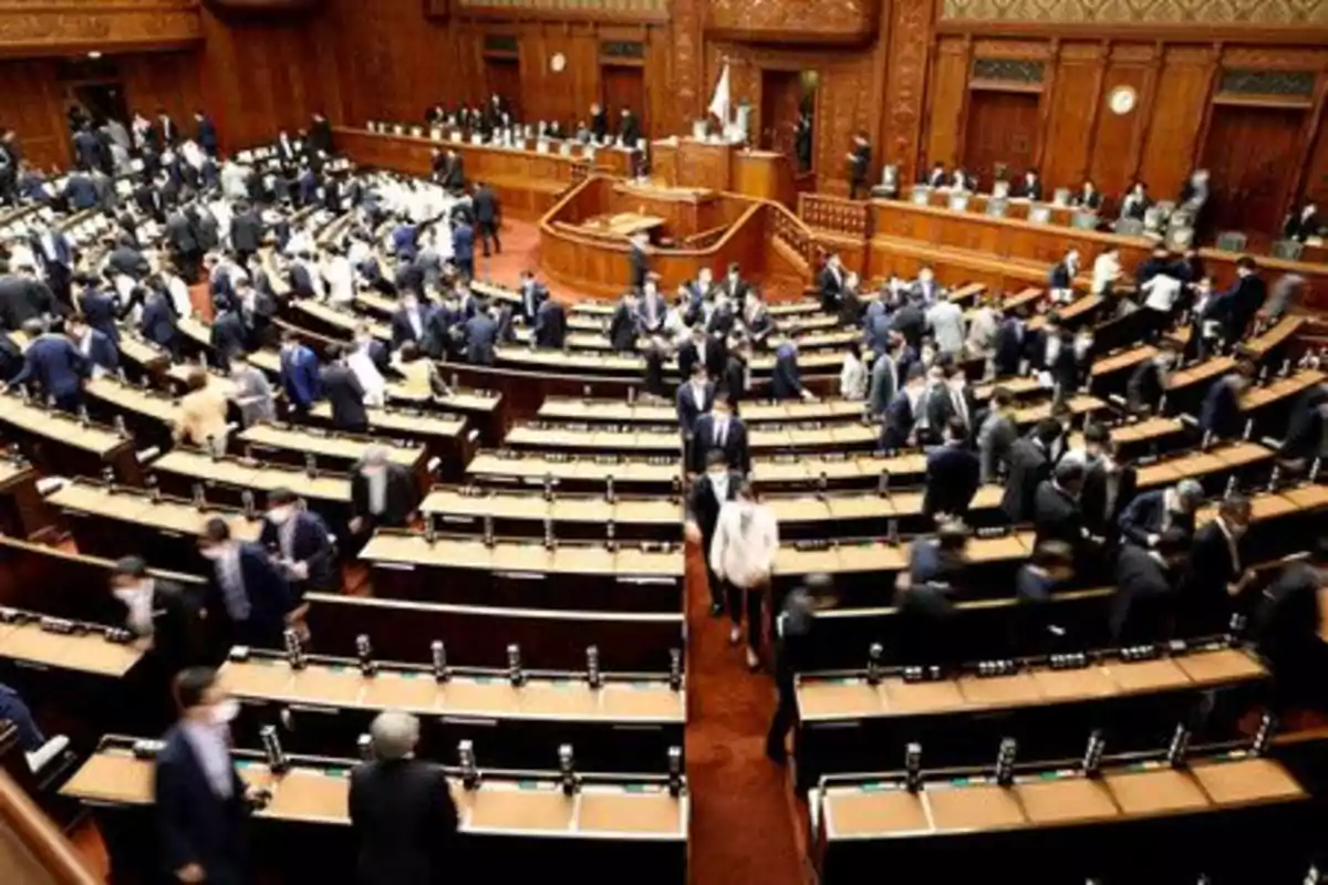 Personas con trajes formales se reúnen y conversan en un gran salón parlamentario de madera Personas con trajes formales se reúnen y conversan en un gran salón parlamentario de madera