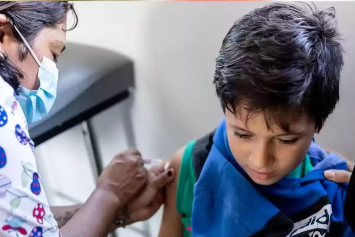 A child receives a vaccine in the arm from a healthcare professional wearing a face mask. A child receives a vaccine in the arm from a healthcare professional wearing a face mask.