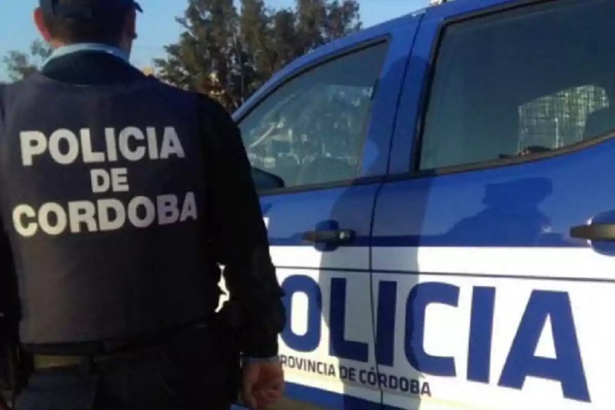 Un policía de Córdoba de espaldas junto a una patrulla azul y blanca Un policía de Córdoba de espaldas junto a una patrulla azul y blanca