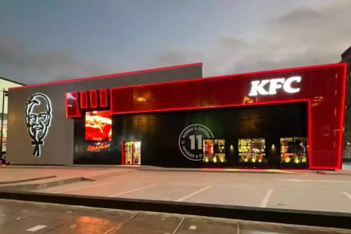 Fachada moderna de un restaurante KFC iluminado por la noche con el logo del Coronel Sanders y luces rojas destacando el edificio Fachada moderna de un restaurante KFC iluminado por la noche con el logo del Coronel Sanders y luces rojas destacando el edificio