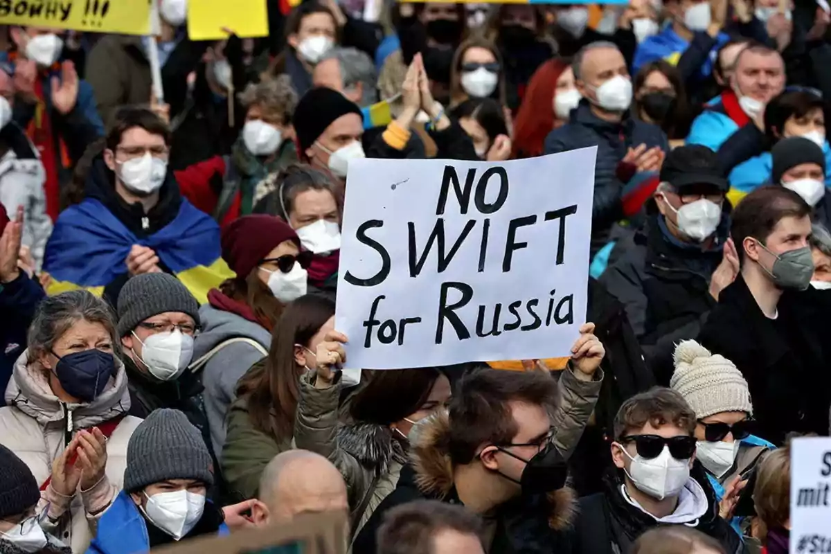 Protesters wearing masks hold signs, one of which says NO SWIFT for Russia. Protesters wearing masks hold signs, one of which says NO SWIFT for Russia.