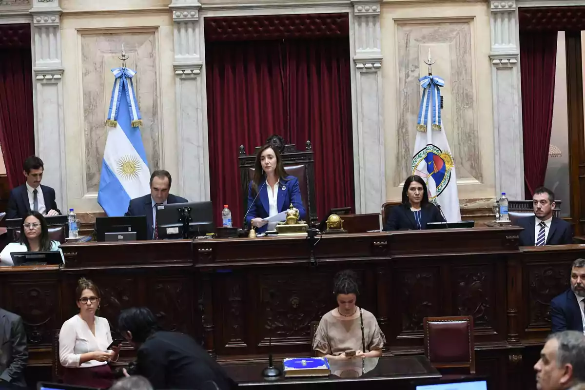 A session in the Argentine Senate with several people seated at their desks and a woman presiding at the center of the platform.