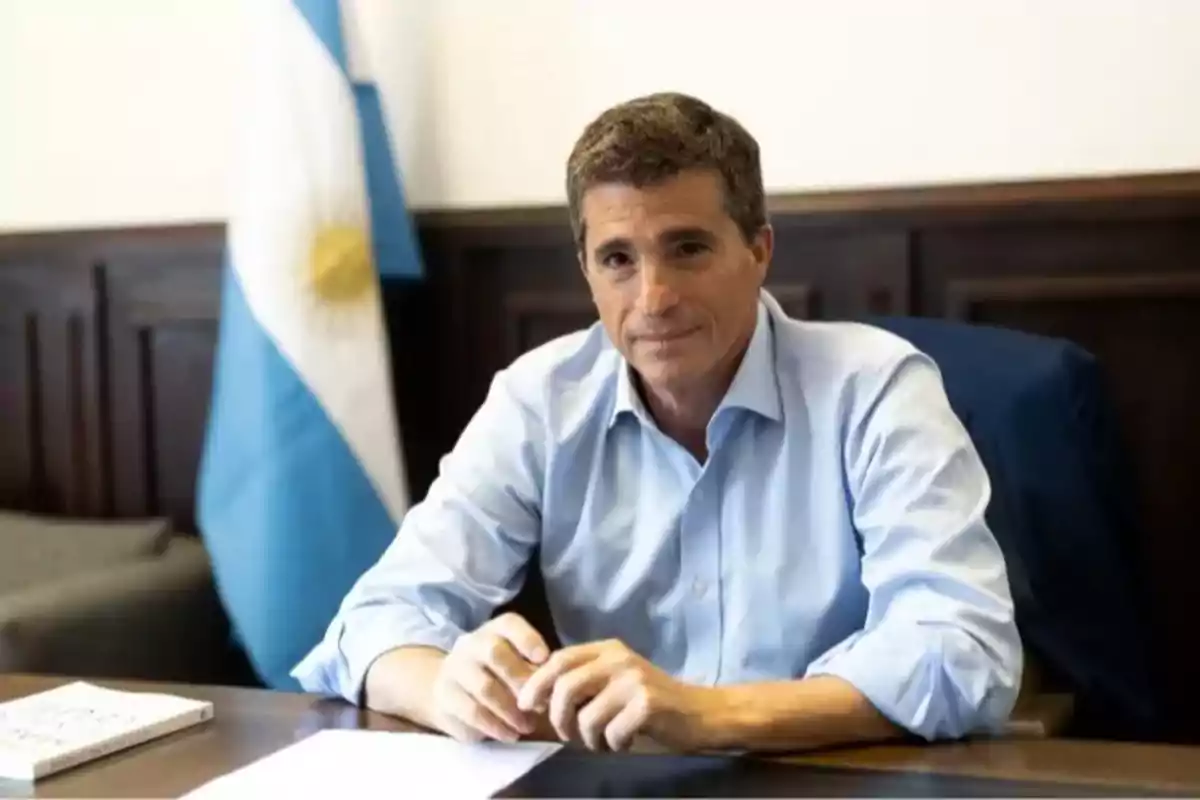 Short-haired, gray-haired man sitting at a desk with an Argentine flag in the background Short-haired, gray-haired man sitting at a desk with an Argentine flag in the background