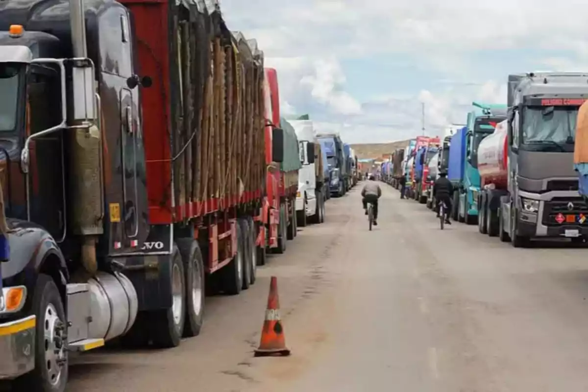 Row of trucks parked on both sides of a road with two people on bicycles riding between them and a traffic cone in the middle of the road Row of trucks parked on both sides of a road with two people on bicycles riding between them and a traffic cone in the middle of the road
