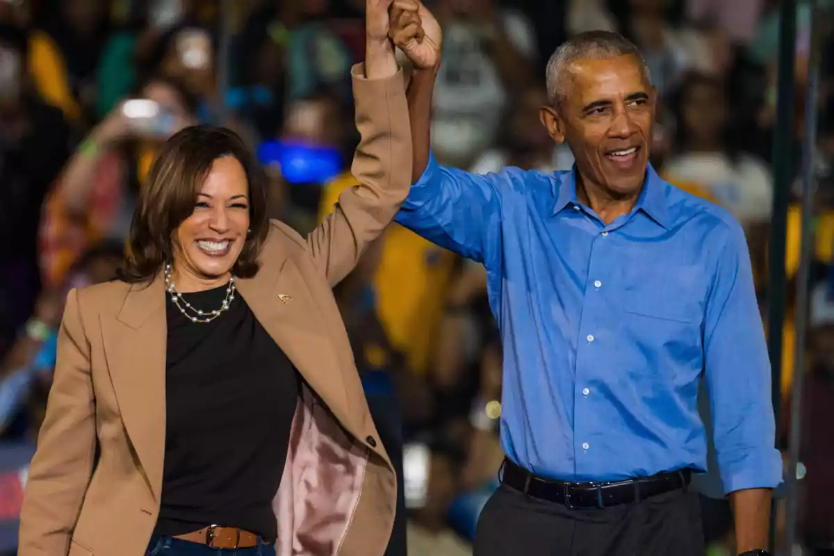 Two people smile and raise their joined hands in celebration in front of a crowd. Two people smile and raise their joined hands in celebration in front of a crowd.