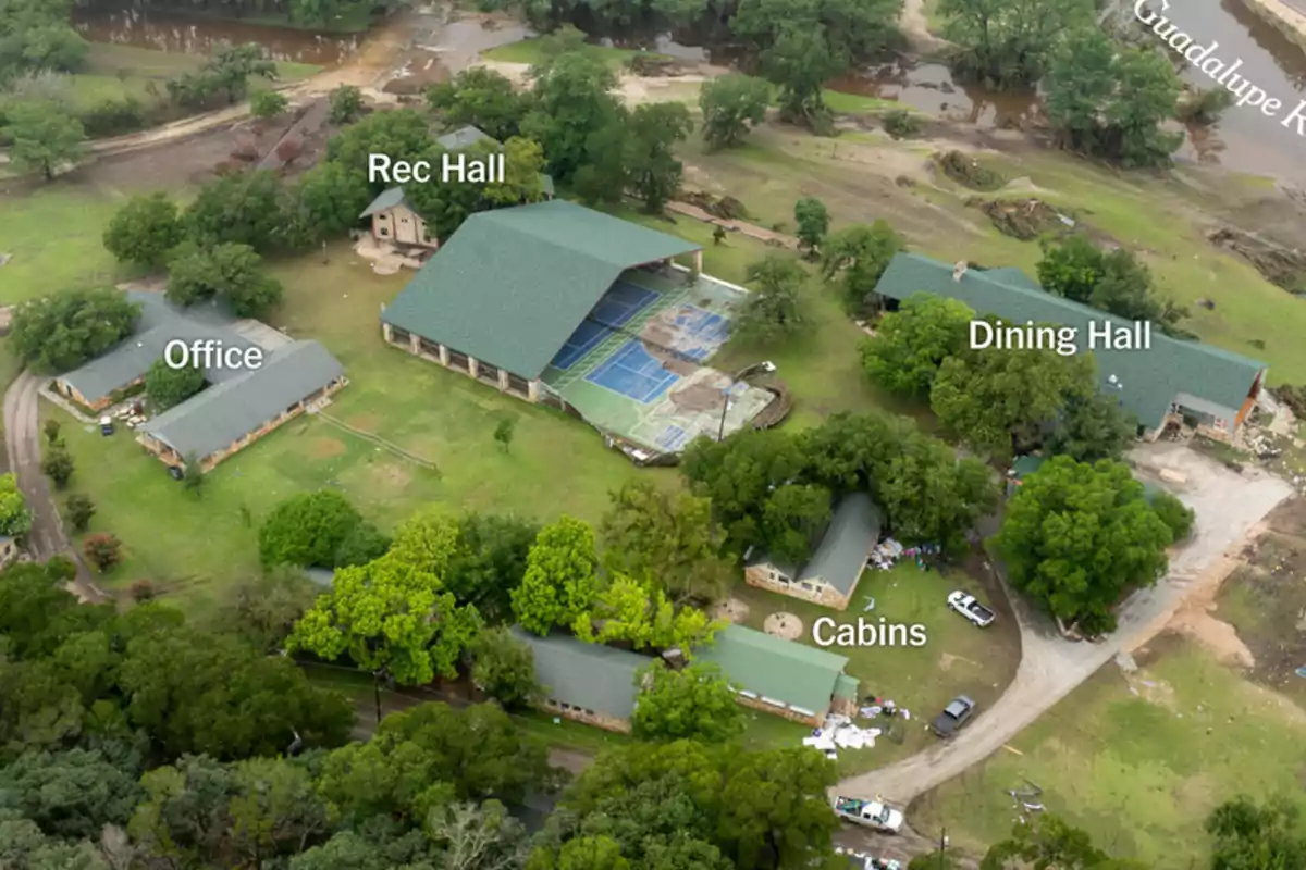Vista aérea de un campamento con edificios etiquetados como Office, Rec Hall, Dining Hall y Cabins rodeados de árboles y áreas verdes junto a un río Vista aérea de un campamento con edificios etiquetados como Office, Rec Hall, Dining Hall y Cabins rodeados de árboles y áreas verdes junto a un río