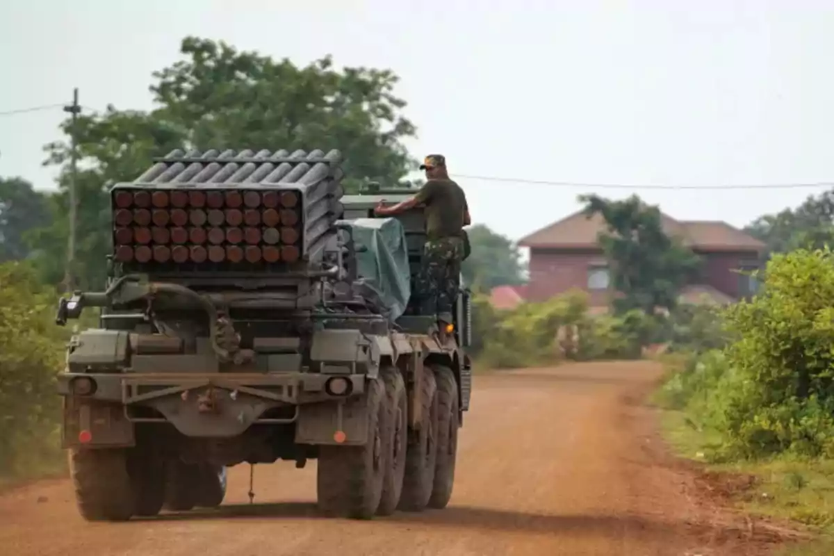 Military vehicle with multiple rocket launcher driving on a dirt road surrounded by vegetation and houses in the background Military vehicle with multiple rocket launcher driving on a dirt road surrounded by vegetation and houses in the background