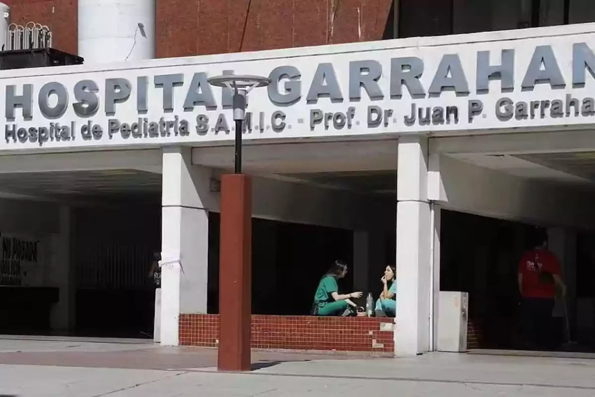 Main entrance of Garrahan Hospital with two people in medical uniforms sitting and talking in the access area Main entrance of Garrahan Hospital with two people in medical uniforms sitting and talking in the access area