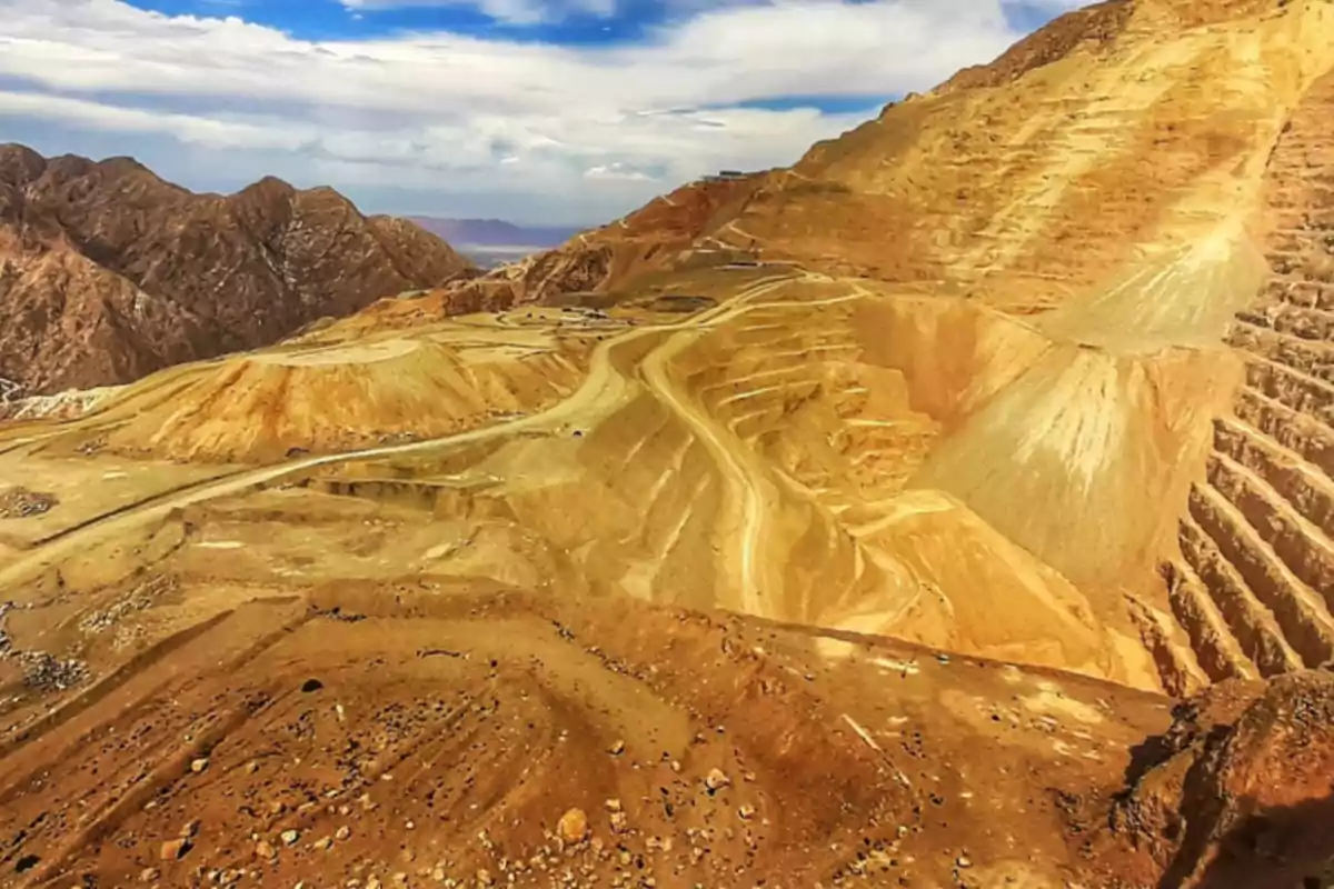 Vista panorámica de una mina a cielo abierto en una zona montañosa con caminos y terrazas escalonadas en el terreno árido