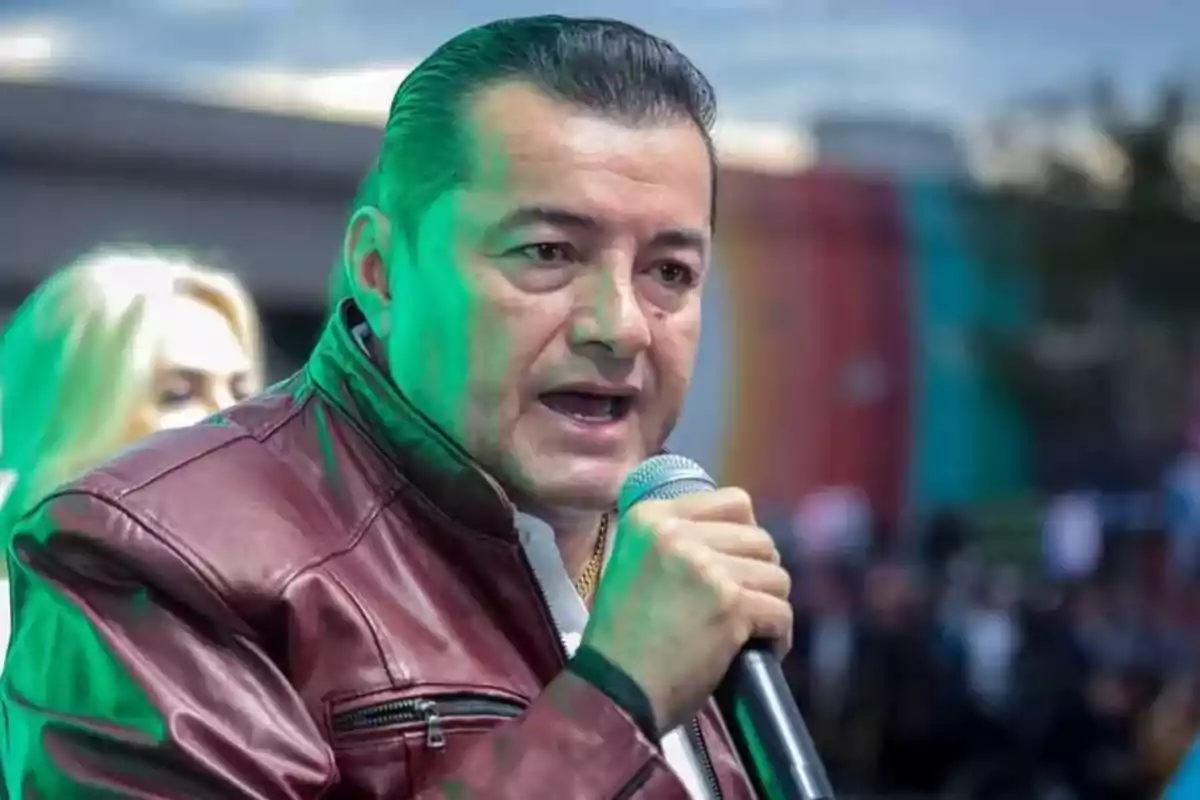 Hombre con chaqueta de cuero roja hablando por un micrófono en un evento al aire libre