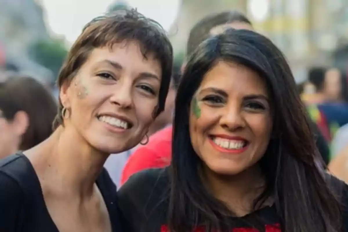 Two women smile as they pose together at an outdoor event, both with decorative face paint and looking happy. Two women smile as they pose together at an outdoor event, both with decorative face paint and looking happy.