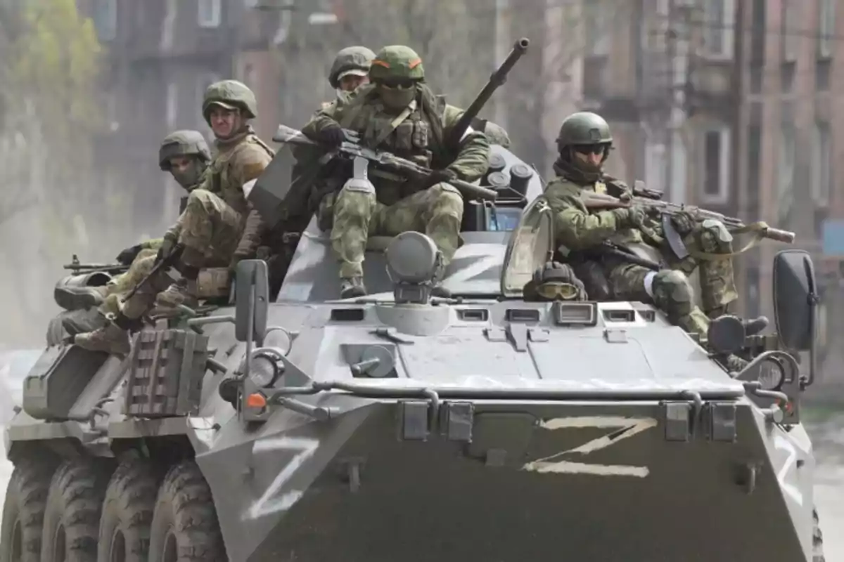 Soldados armados con uniforme militar y casco viajan sobre un vehículo blindado en una zona urbana Soldados armados con uniforme militar y casco viajan sobre un vehículo blindado en una zona urbana