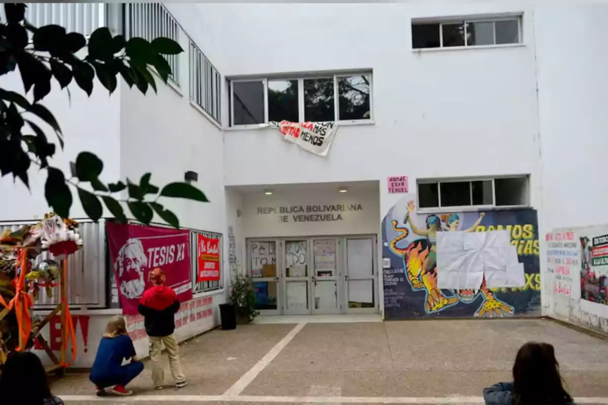 Facade of a white building with posters and murals, people observing, and a banner hanging in the upper window Facade of a white building with posters and murals, people observing, and a banner hanging in the upper window