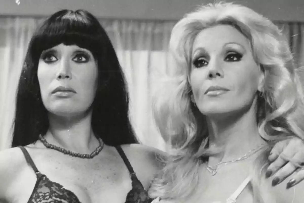 Dos mujeres posan juntas en una fotografía en blanco y negro, una de cabello oscuro y la otra rubia, ambas con expresión seria y vistiendo lencería Dos mujeres posan juntas en una fotografía en blanco y negro, una de cabello oscuro y la otra rubia, ambas con expresión seria y vistiendo lencería