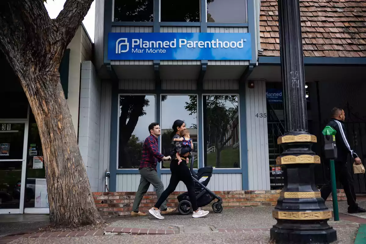 Una pareja camina con un cochecito y un niño pequeño frente a una clínica de Planned Parenthood en una calle urbana Una pareja camina con un cochecito y un niño pequeño frente a una clínica de Planned Parenthood en una calle urbana