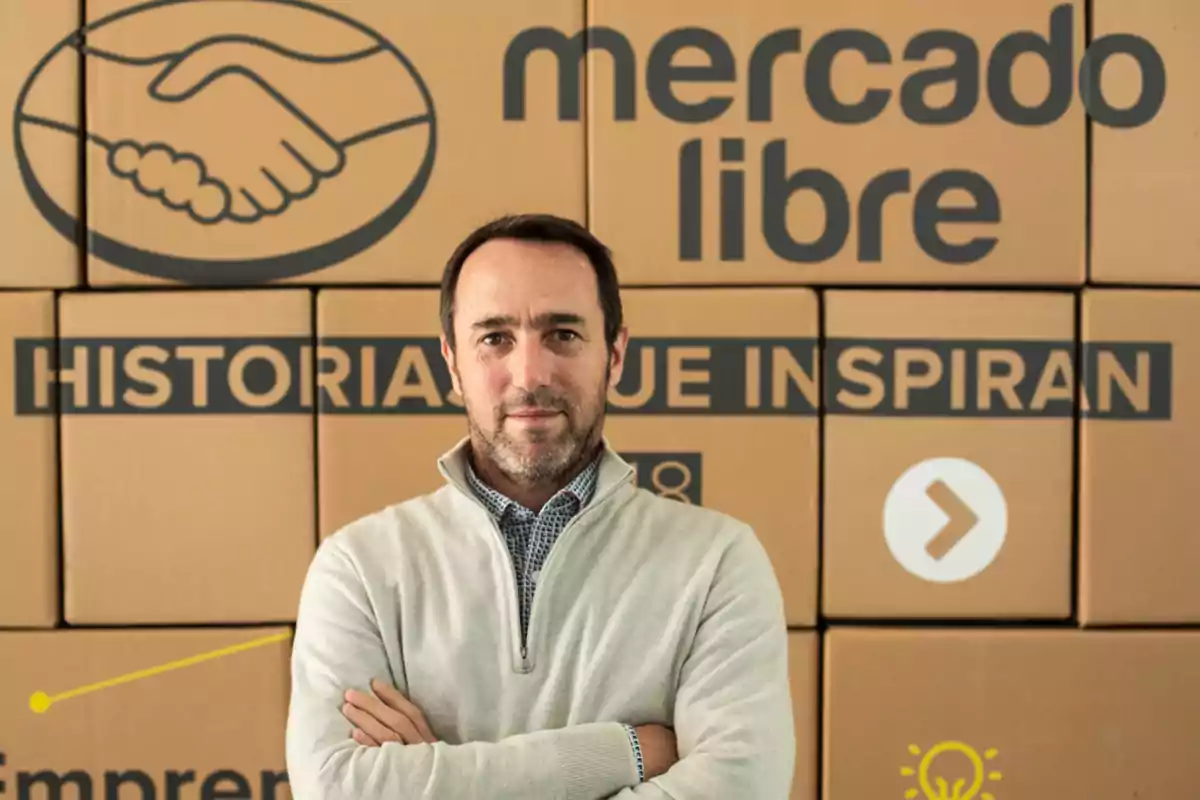Short-haired, bearded man wearing a light sweater posing in front of cardboard boxes with the Mercado Libre logo and name.