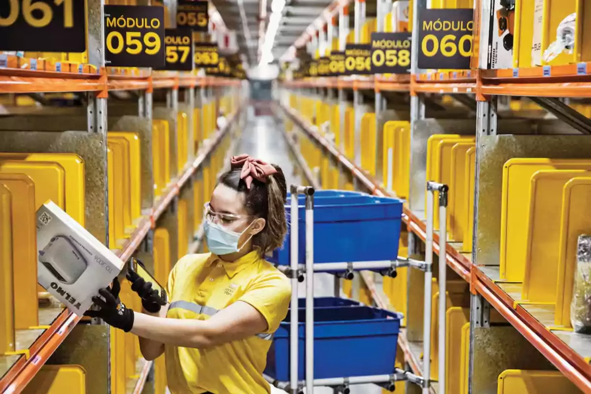 Trabajadora con cubrebocas y gafas de protección escaneando una caja en un almacén con estantes amarillos y contenedores azules