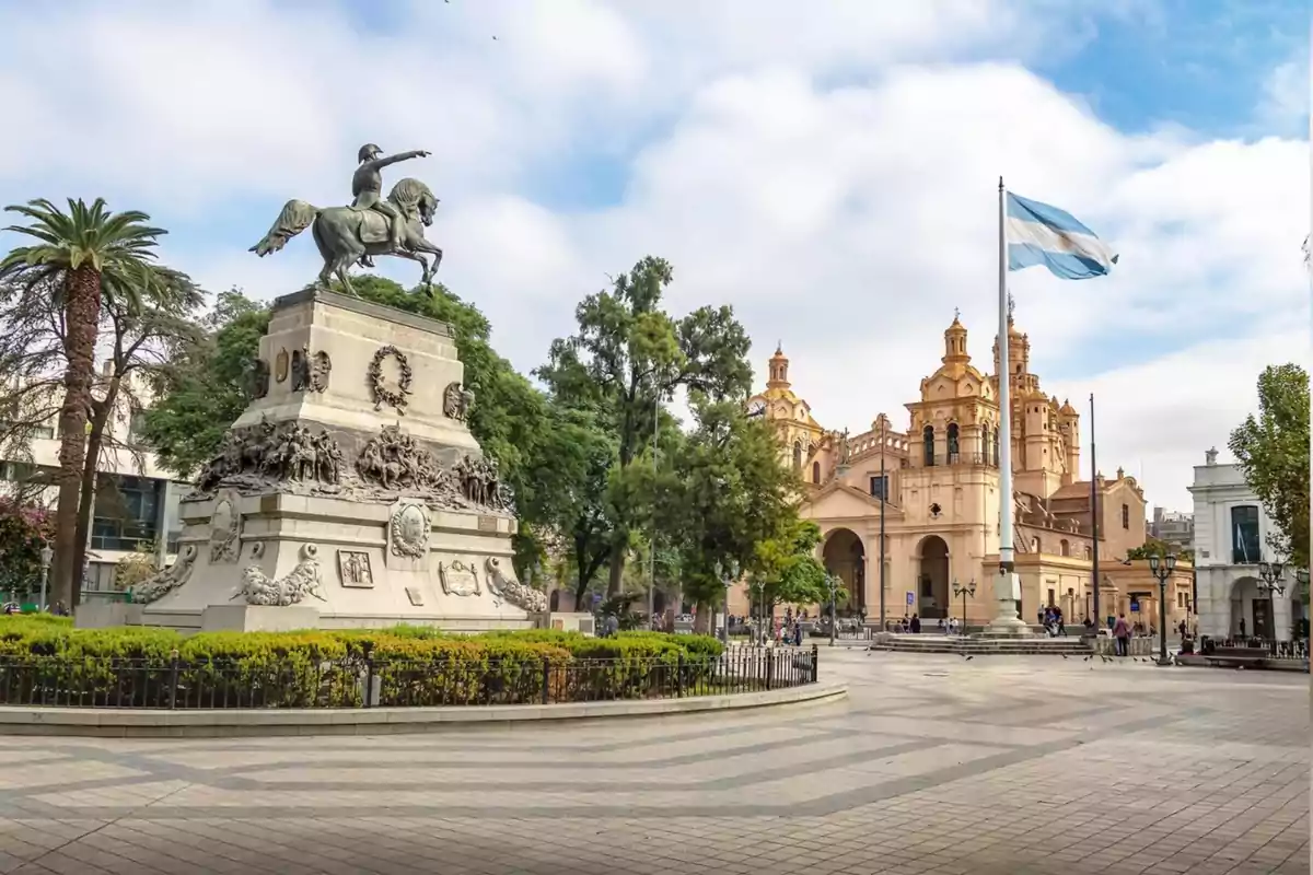 Plaza céntrica con monumento ecuestre, bandera argentina y una catedral al fondo en un día soleado