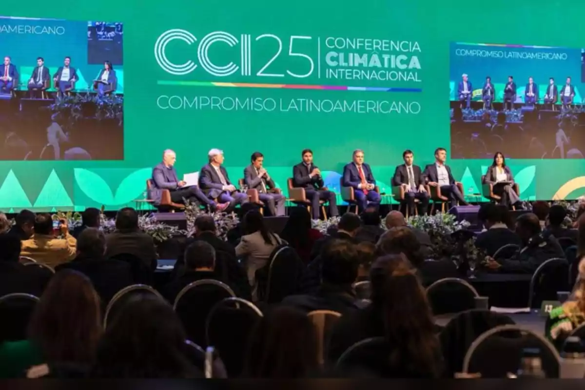 Un grupo de panelistas sentados en el escenario de una conferencia climática internacional frente a una audiencia, con una gran pantalla verde de fondo que muestra el nombre del evento y el lema compromiso latinoamericano