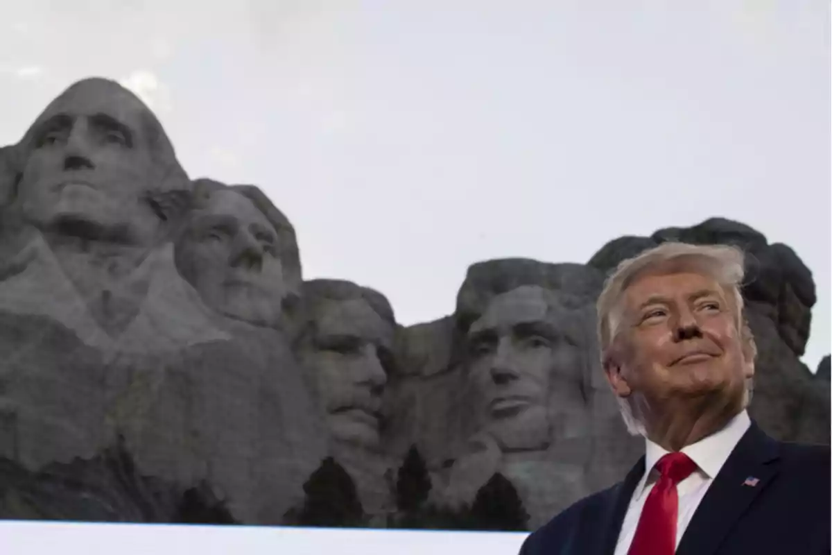 Un hombre de traje y corbata roja posando frente al monumento del Monte Rushmore al atardecer
