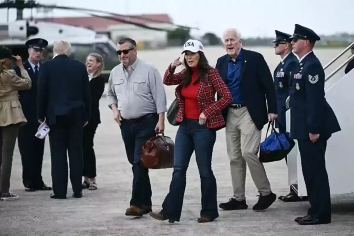 Varias personas caminan en una pista de aterrizaje junto a un helicóptero y personal militar Varias personas caminan en una pista de aterrizaje junto a un helicóptero y personal militar