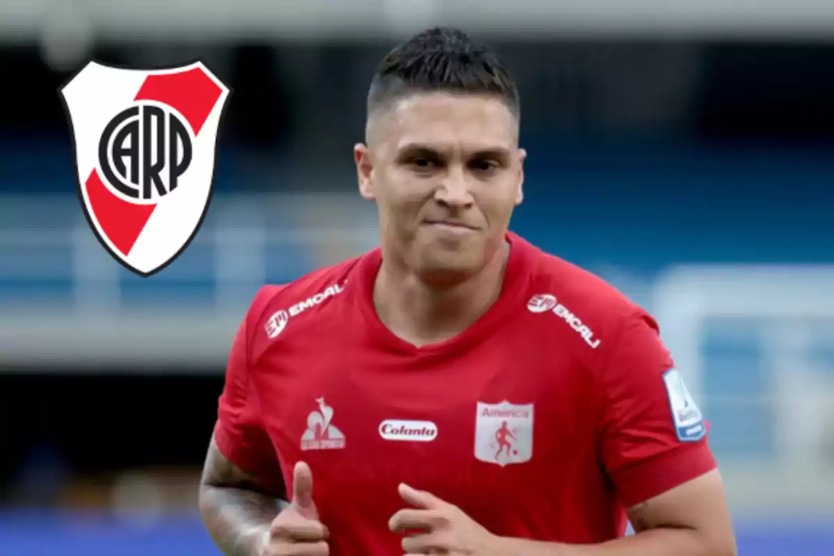 Futbolista con camiseta roja de América de Cali corriendo en un estadio con el escudo de River Plate al fondo
