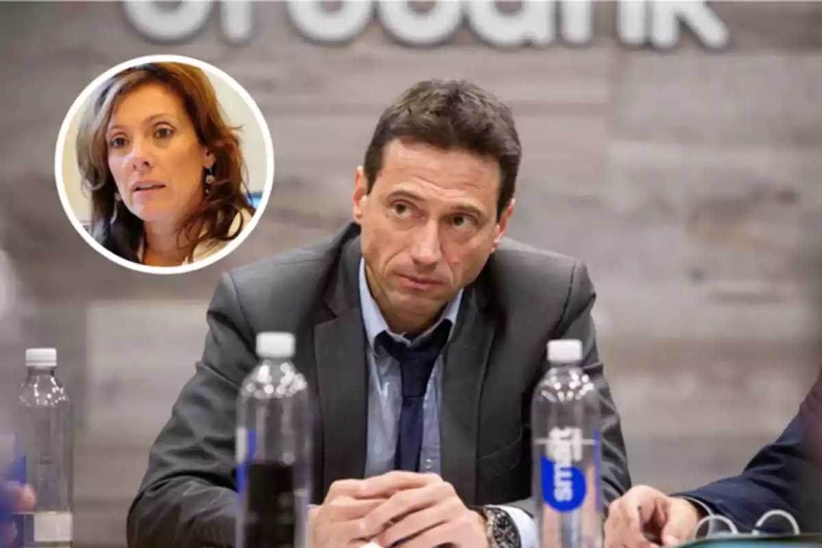 Hombre con expresión seria sentado en una mesa de reuniones con botellas de agua y una mujer en un recuadro circular en la esquina superior izquierda