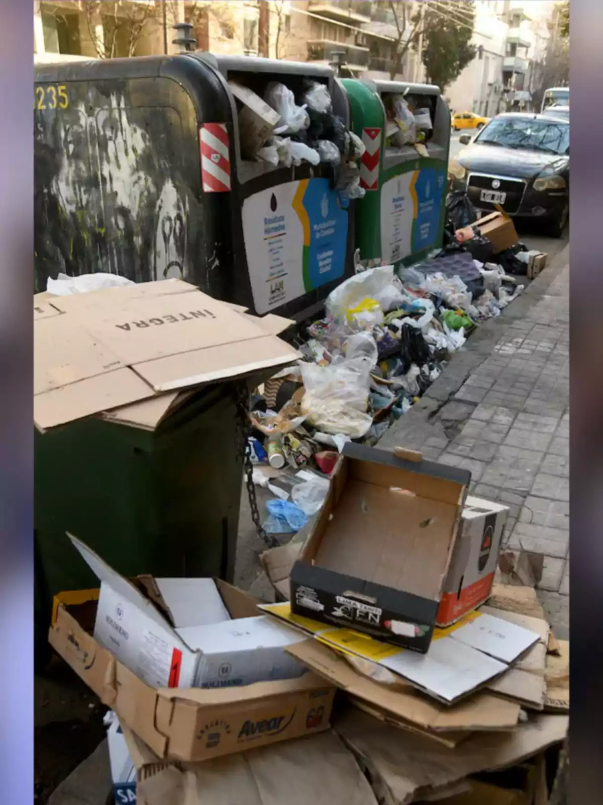 Overflowing trash bins with bags and boxes stacked on the sidewalk of an urban street Overflowing trash bins with bags and boxes stacked on the sidewalk of an urban street