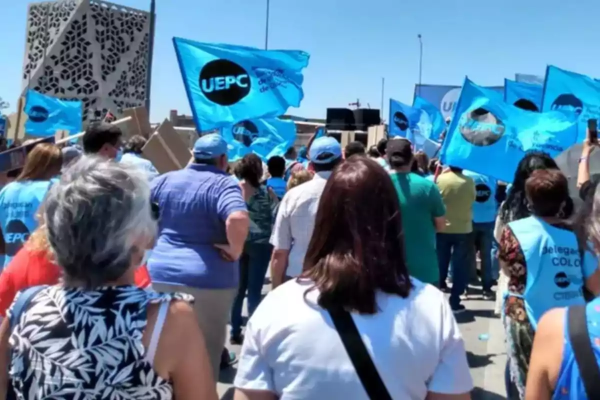 Un grupo de personas participa en una manifestación portando banderas celestes de la UEPC bajo un cielo despejado