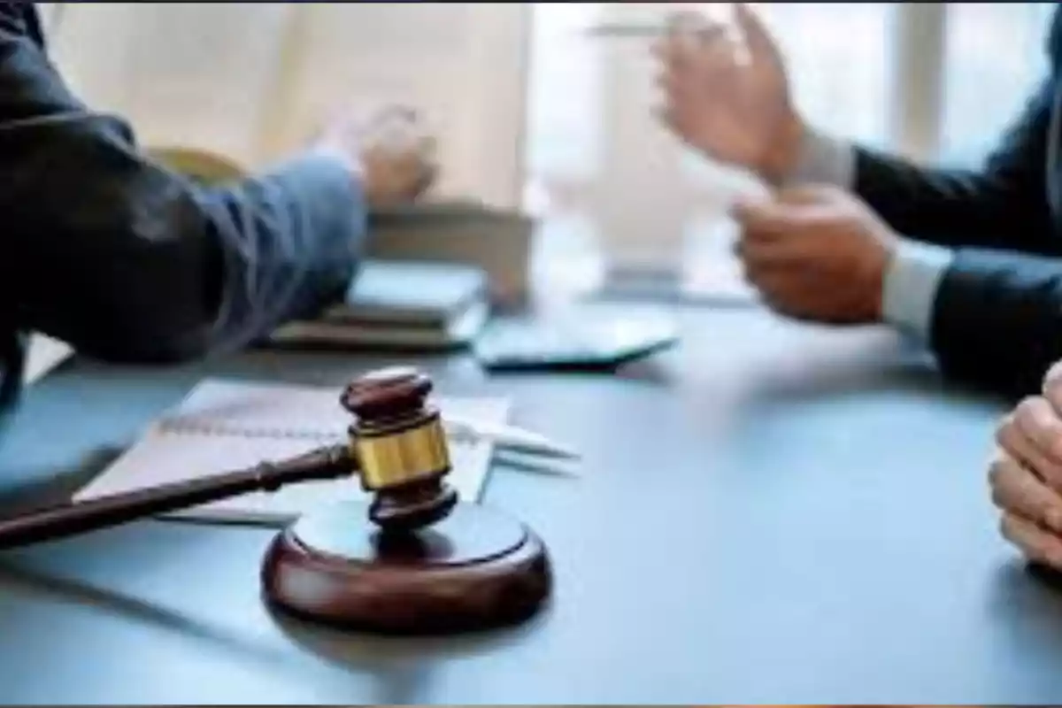 Dos personas con trajes conversan en una mesa de oficina con un mazo de juez y documentos sobre la superficie Dos personas con trajes conversan en una mesa de oficina con un mazo de juez y documentos sobre la superficie