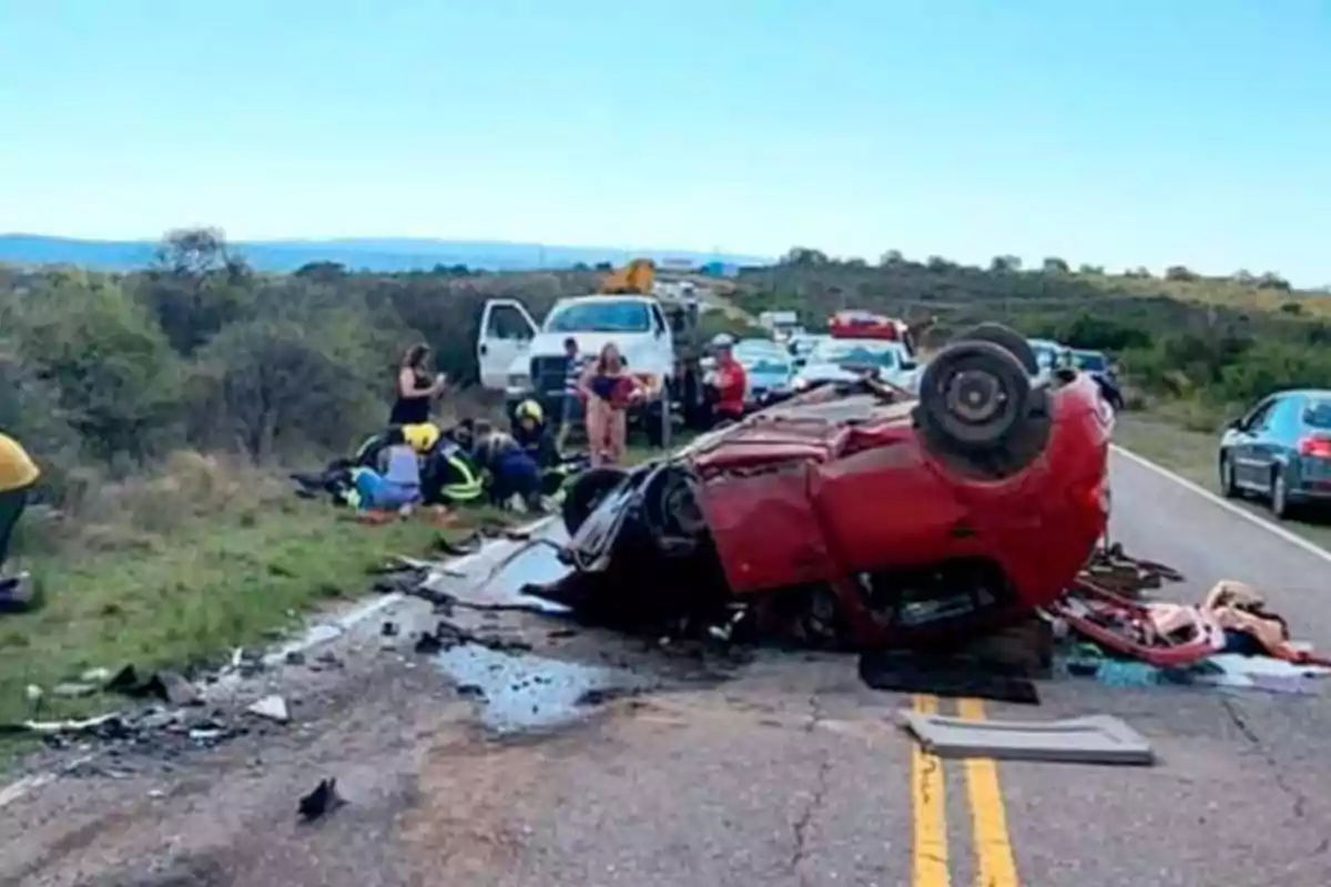 Auto rojo volcado en medio de una carretera con varios rescatistas y vehículos de emergencia atendiendo la escena del accidente Auto rojo volcado en medio de una carretera con varios rescatistas y vehículos de emergencia atendiendo la escena del accidente